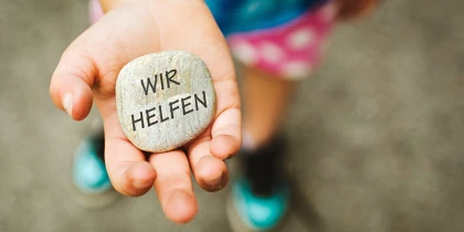 Child holding a stone with “WE HELP” written on it